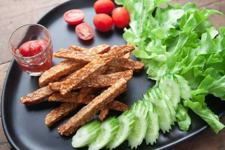 Fried tempeh on a black plate with salad ingredients