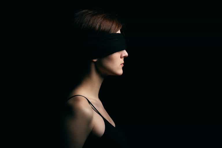 A woman blindfolded in a black eye mask, with black background