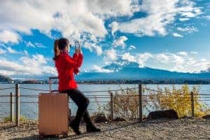 Traveler in red jacket taking a photo near a lake with blue skies above