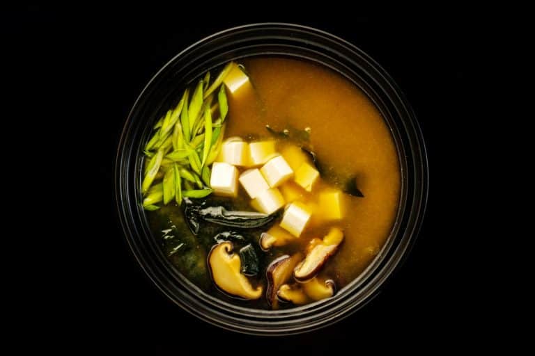 Bowl of miso soup with tofu and noodles on dark background