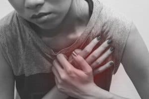 Black and white picture of young woman holding hands over a painful heart